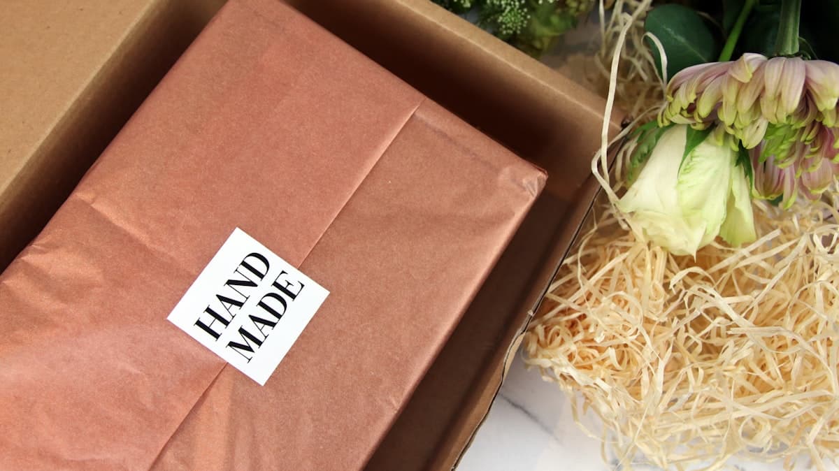 Square sticker with hand-made design applied to seal tissue paper in a box