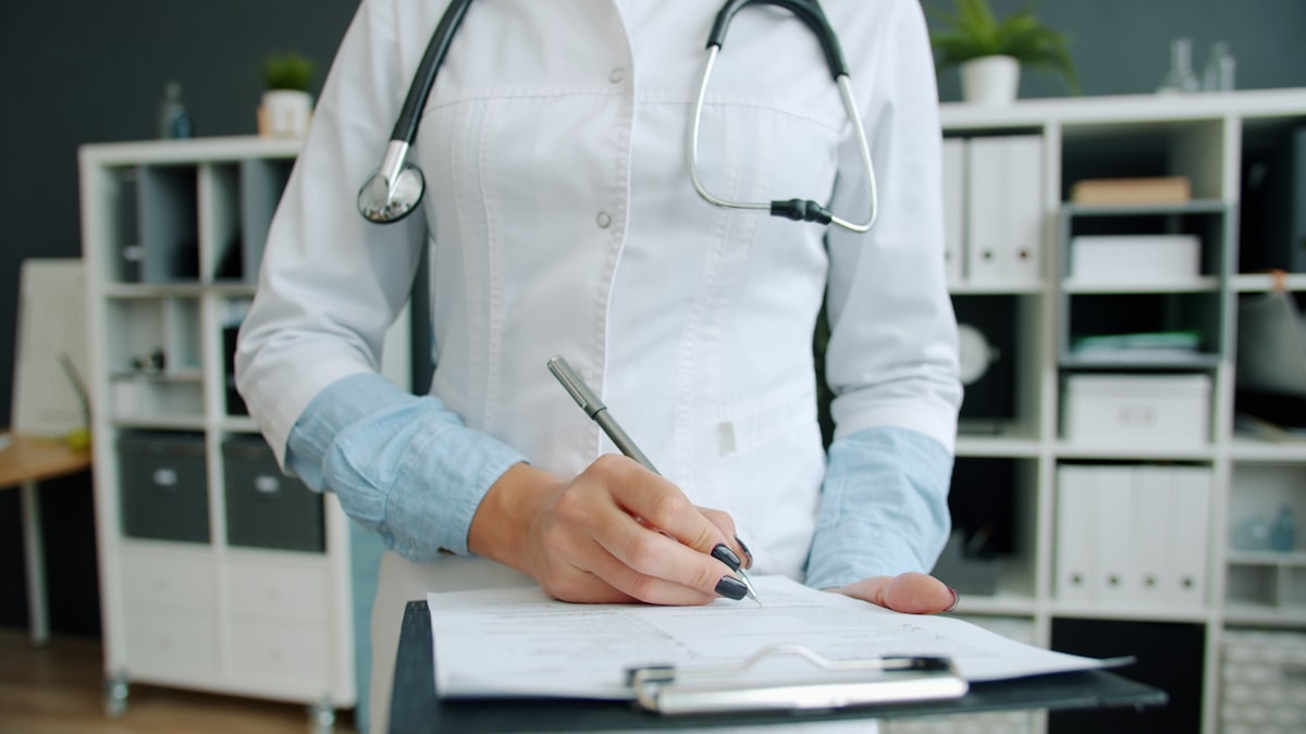 Close-up shot of hand of doctor writing in patient's medical records ticking symptoms working in hospital office. Medicine, paperwork and profession concept.